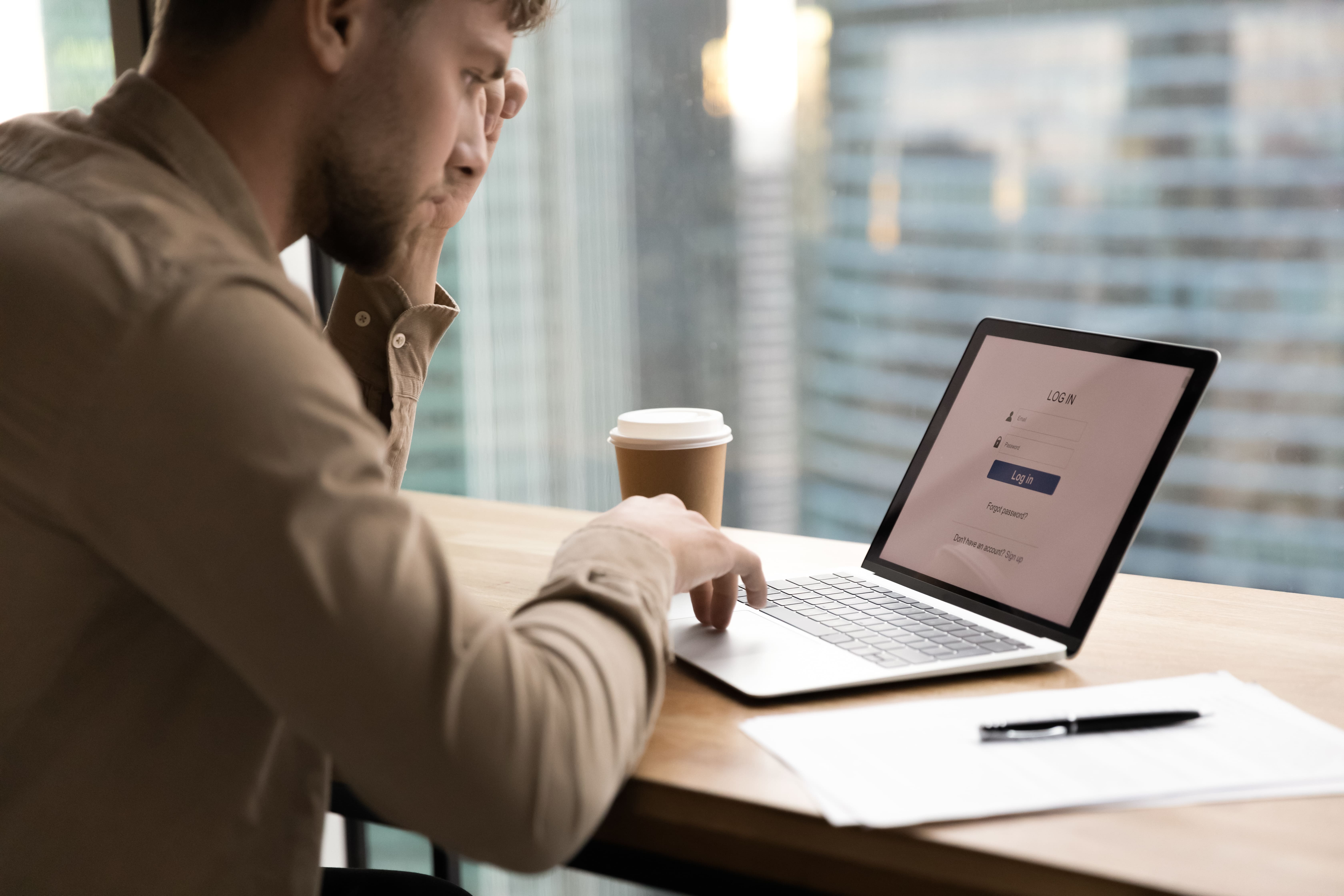 Young man sitting at desk with laptop, appearing thoughtful while considering business setup